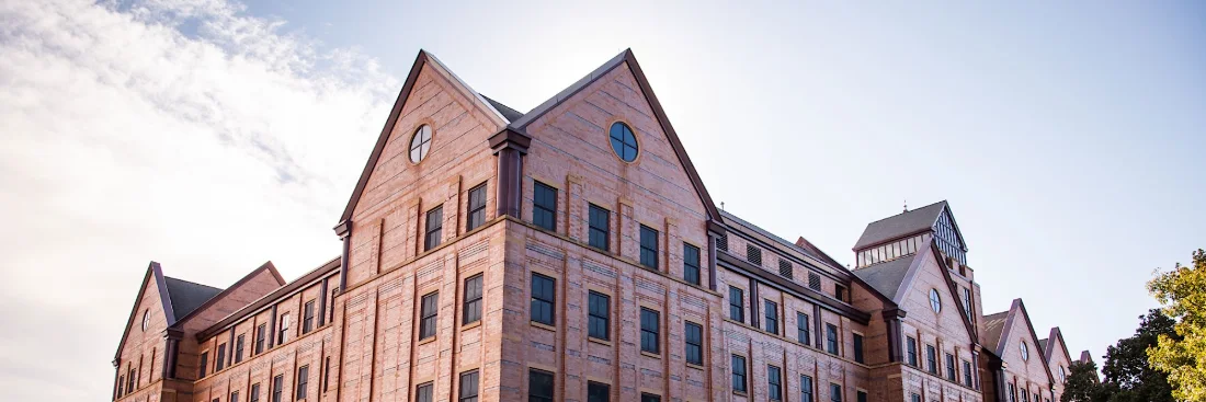 A tall red-brick building with steep gabled roofs and round windows against a bright sky.