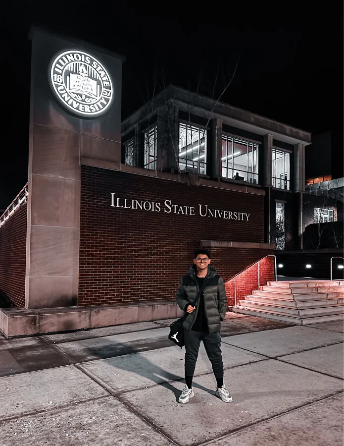 Salman smiling at night in front of a brick building with the lit Illinois State University seal and lettering.