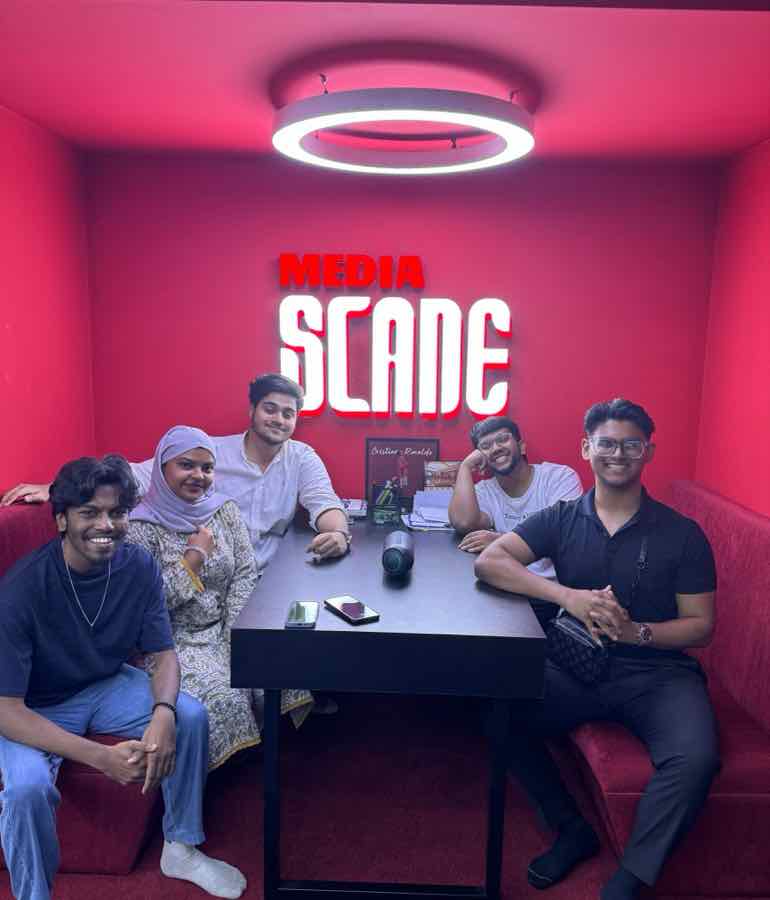 Salman and four Scane Media teammates smiling around a table in a red booth under a lit Media Scane sign.